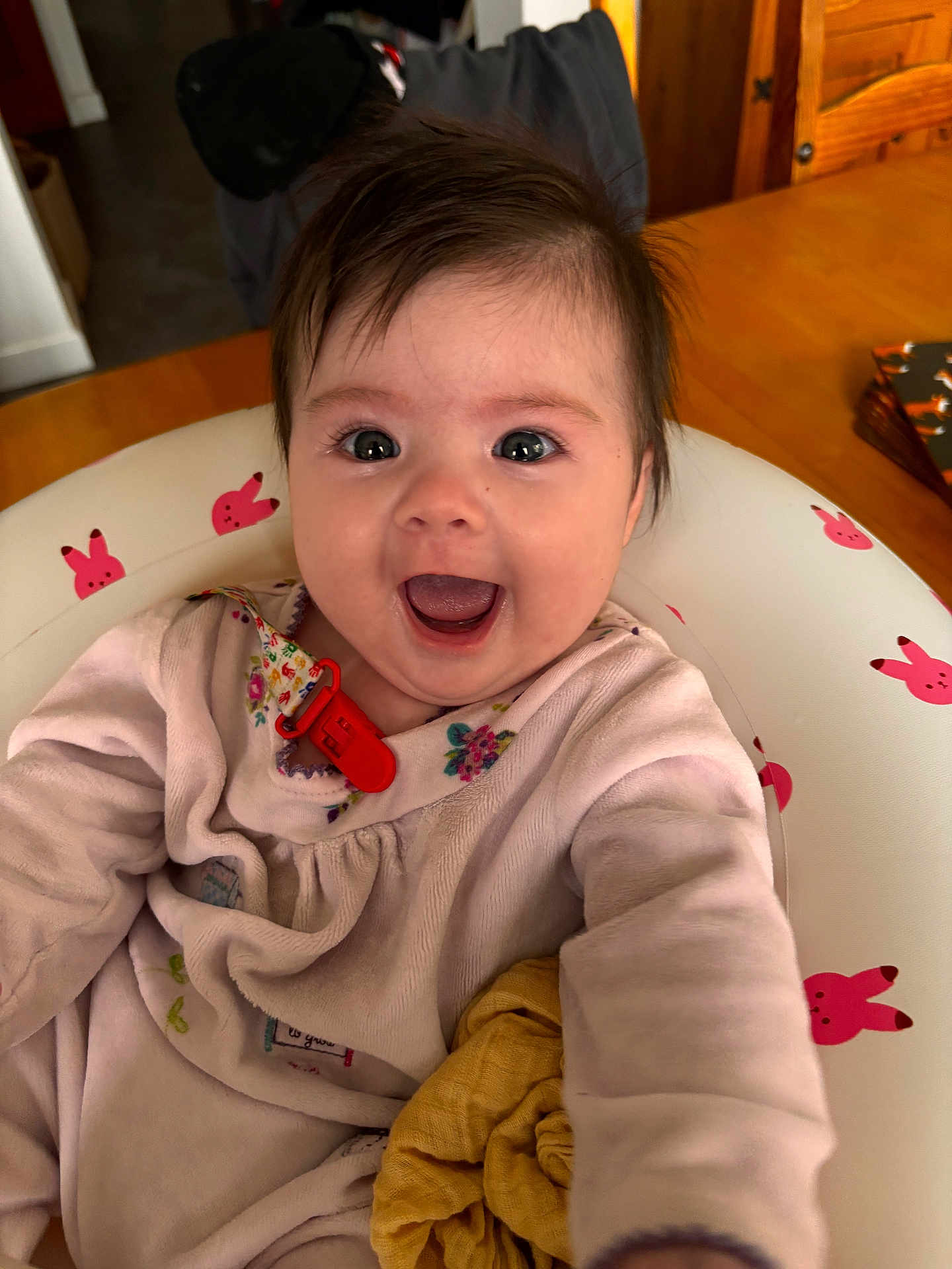 Lyra is registered to the contest to win money with this photo: baby, child, smiling, happy, face, eyes, mouth, clothing, pink, floral, bunny_pattern, seat, indoor, table, wood, blanket, cute, portrait, infant, cozy