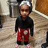 child, costume, mickey_mouse, indoor, floor, wood, slippers, pink, black, red, white, face, expression, trash_can, door, wall, person, standing, clothing, room