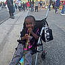 child, stroller, drink, festival, people, street, outdoor, happy, smiling, sneakers, bag, food_stand, crowd, casual_clothing, daytime, pavement, urban, event, fun, celebration