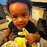 Kordae is registered to the contest to win money with this photo: toddler, child, curly_hair, snack, indoor, carpet, tablet, plastic_container, black_shirt, yellow_towel, hand, face, food, person, cute, baby, room, floor, sitting, curious