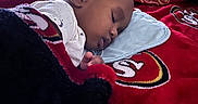Kordae is registered to the contest to win money with this photo: baby, sleeping, blanket, bed, pillow, indoor, child, cozy, rest, face, curly_hair, red, black, white, clothing, comfort, peaceful, portrait, infant, toddler