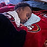 baby, sleeping, blanket, bed, pillow, indoor, child, cozy, rest, face, curly_hair, red, black, white, clothing, comfort, peaceful, portrait, infant, toddler