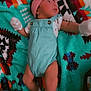 baby, infant, blanket, headband, mittens, romper, socks, colorful, patterned_blanket, lying_down, cute, child, soft_toys, indoor, portrait, small_person, pink_bow, turquoise, cozy, resting
