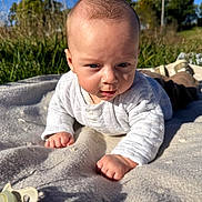 Bentley is registered to the contest to win money with this photo: baby, infant, blanket, outdoor, grass, sunlight, sky, clothing, face, hand, nature, daylight, cute, young_child, field, head, expression, portrait, toddler, reaching