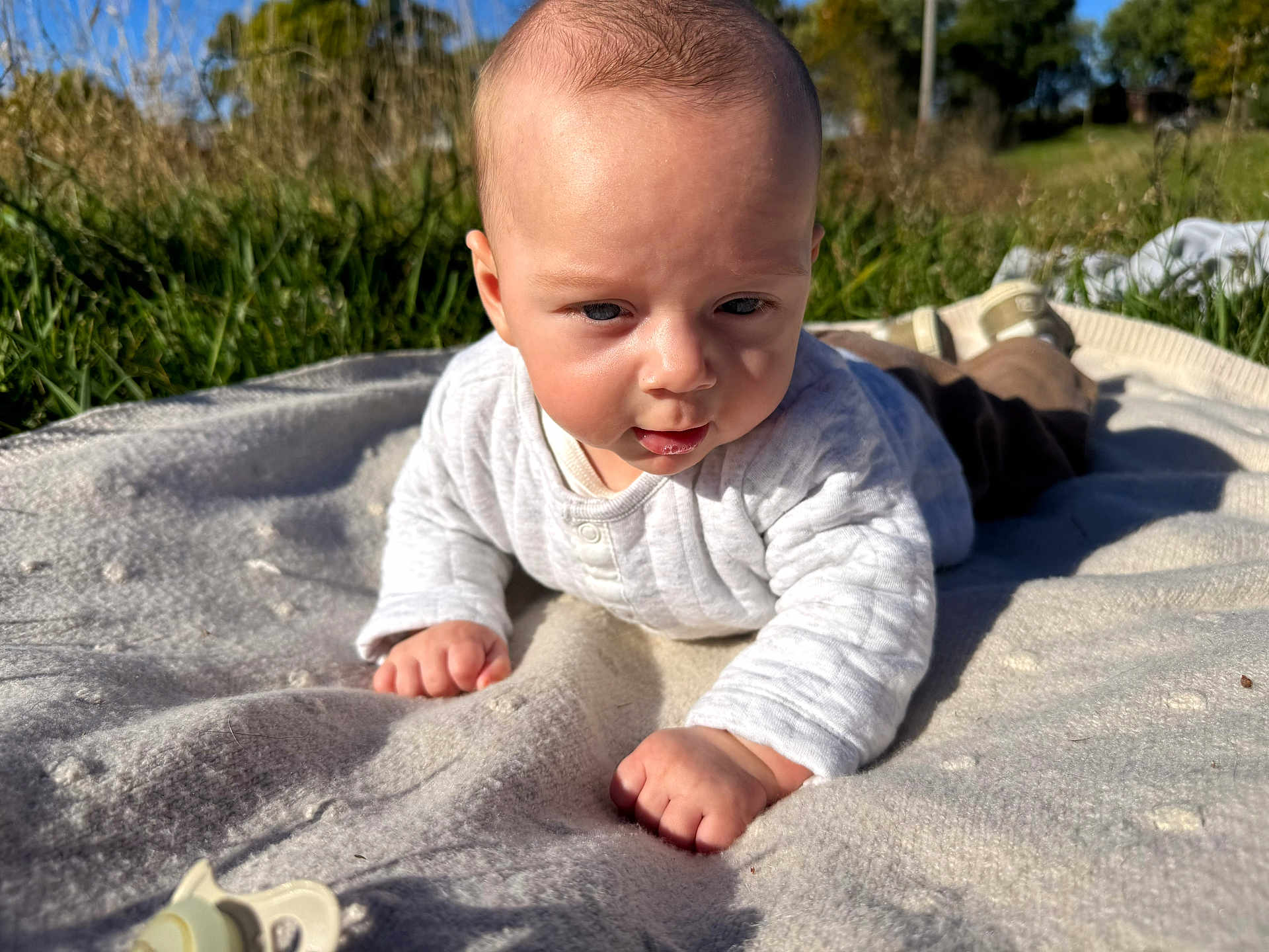 Bentley is registered to the contest to win money with this photo: baby, infant, blanket, outdoor, grass, sunlight, sky, clothing, face, hand, nature, daylight, cute, young_child, field, head, expression, portrait, toddler, reaching
