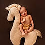 baby, newborn, smile, sleeping, cushion, plush_toy, horse, soft_texture, infant, bare_chest, brown_background, peaceful, cute, child, portrait, relaxing, cozy, indoor, resting, toy
