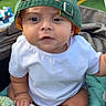 baby, child, infant, portrait, sitting, baseball_cap, green_hat, white_shirt, plush_toy, sheep_toy, blanket, outdoor, sports_field, spectators, chairs, daylight, close_up, wide_eyes, cute, family_photo