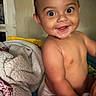 baby, child, infant, smiling, happy, portrait, sitting, indoors, blanket, bed, home, face, eyes, hair, bare_shoulders, playful, close_up, photograph, cozy, adorable