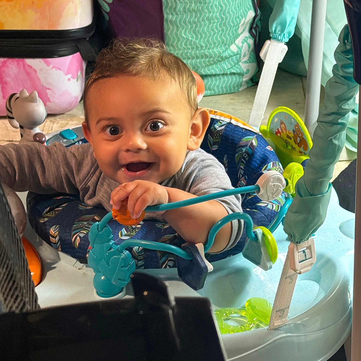 Kai is registered to the contest to win money with this photo: baby, child, infant, smiling, happy, portrait, face, eyes, indoors, playroom, activity_center, baby_jumper, toy, colorful, seated, clothing, cushions, household, daylight, photography