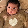adorable, baby, baby_clothing, blanket, child, close_up, cozy, curly_hair, cute, face, heart_pattern, indoors, infant, knitted_sweater, looking_at_camera, portrait, resting, smiling, soft_texture, warm
