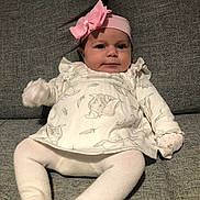 Olivia-May is registered to the contest to win money with this photo: baby, infant, pink_bow, headband, white_clothing, mittens, elephant_print, couch, sofa, grey_fabric, tights, cute, indoor, portrait, child, young, sitting, cozy, face, expression