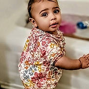Mae'Ahna is registered to the contest to win money with this photo: baby, child, couch, curly_hair, cute, earrings, fashion, floor, floral_outfit, full_body, furniture, indoor, living_room, patterned_clothing, portrait, smiling, standing, toddler, wall, wide_eyes