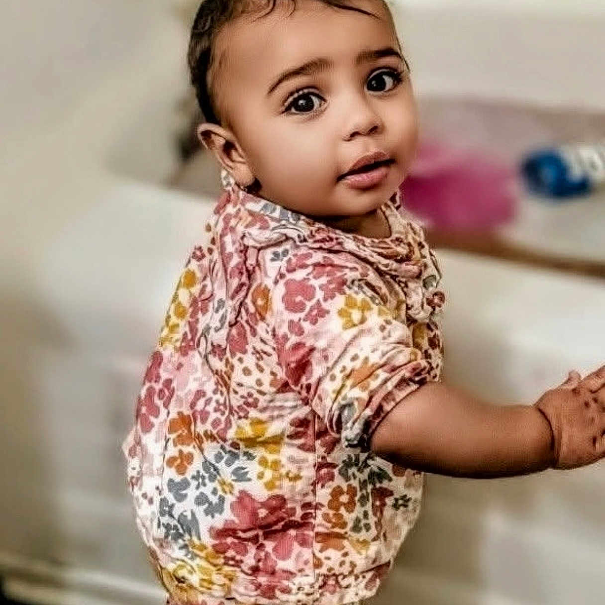 Mae'Ahna is registered to the contest to win money with this photo: baby, child, couch, curly_hair, cute, earrings, fashion, floor, floral_outfit, full_body, furniture, indoor, living_room, patterned_clothing, portrait, smiling, standing, toddler, wall, wide_eyes