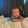 Armand is registered to the contest to win money with this photo: baby, infant, child, portrait, face, sitting, lying_down, blanket, bed, bedding, clothing, green_shirt, gray_collar, indoor, bedroom, curtains, furniture, cozy, photography, expression