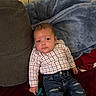 baby, child, infant, portrait, sitting, couch, blanket, plaid_shirt, jeans, pacifier, face, eyes, brown_hair, indoor, home, furniture, textile, red_cushion, blue_blanket, casual_clothing