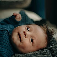 Jules a rejoint le concours — aidez-le/la à gagner de superbes lots ! baby, infant, face, eyes, smile, hair, blue_sweater, blanket, texture, portrait, lying_down, cozy, soft_light, cute, child, skin, closeup, indoors, young, expression