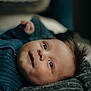 baby, infant, face, eyes, smile, hair, blue_sweater, blanket, texture, portrait, lying_down, cozy, soft_light, cute, child, skin, closeup, indoors, young, expression