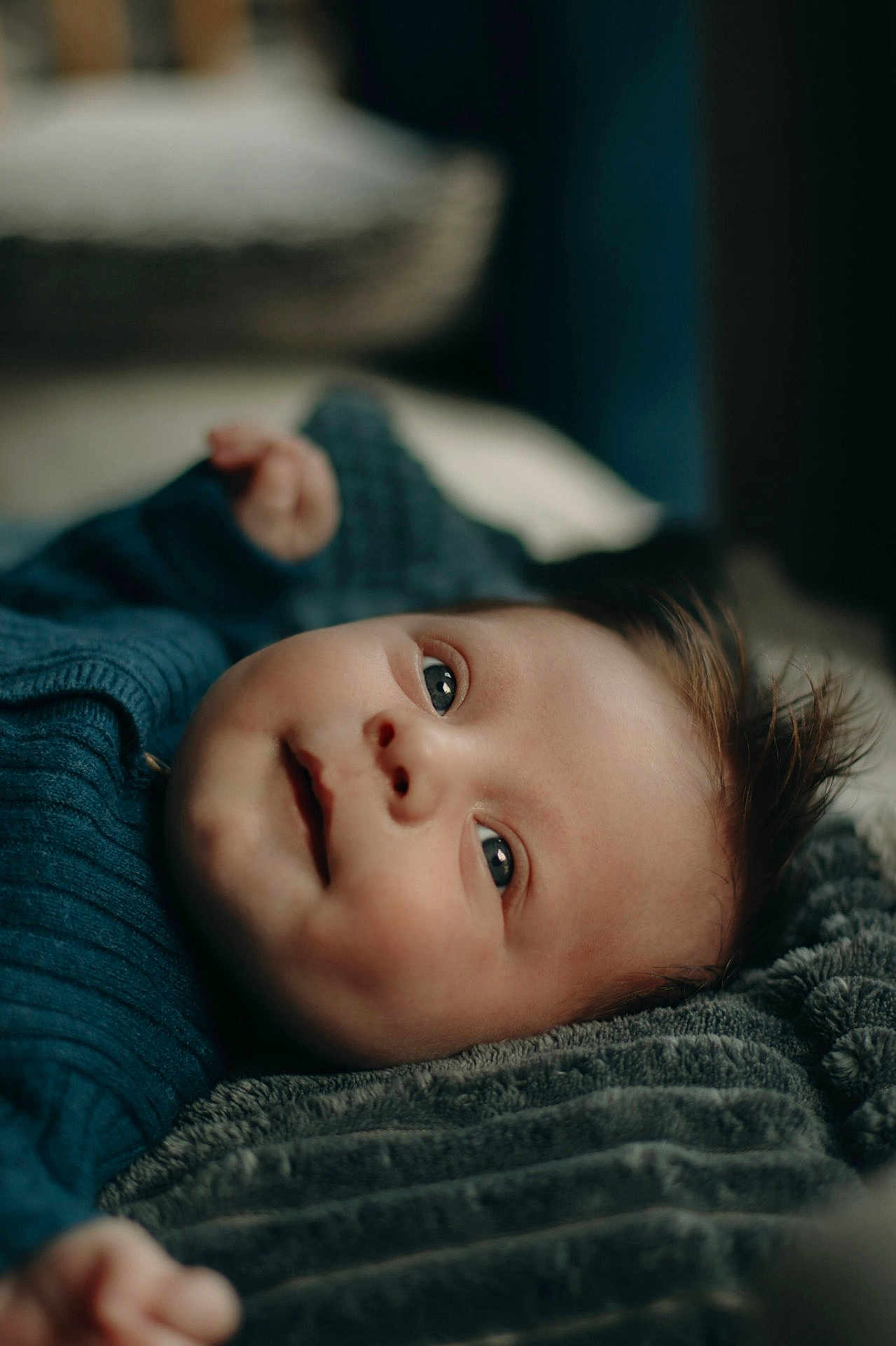 Jules a rejoint le concours — aidez-le/la à gagner de superbes lots ! baby, infant, face, eyes, smile, hair, blue_sweater, blanket, texture, portrait, lying_down, cozy, soft_light, cute, child, skin, closeup, indoors, young, expression