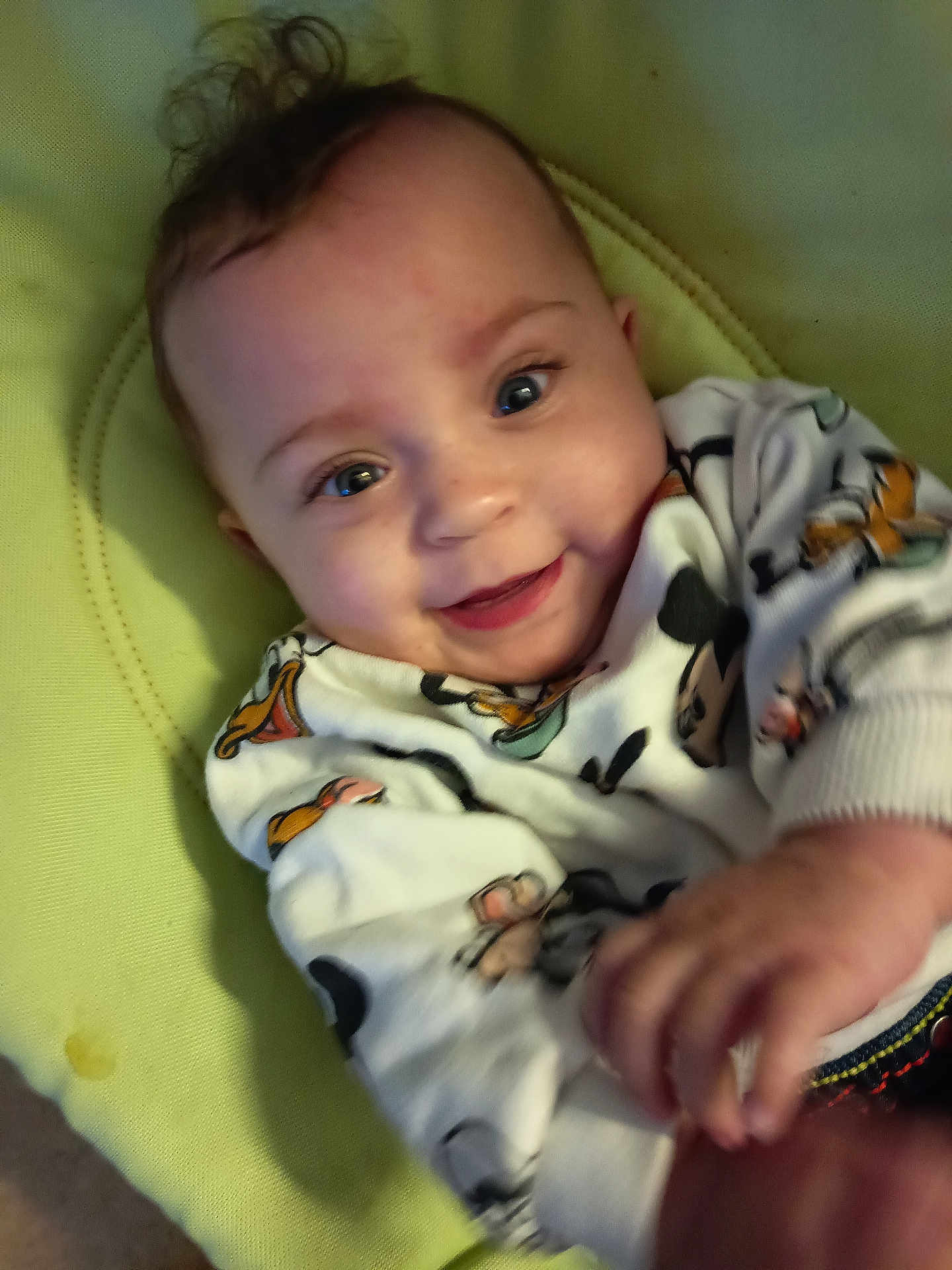 Anaëlle participe au concours pour gagner de l'argent avec cette photo : baby, infant, smiling, face, hand, curly_hair, blue_eyes, clothing, mickey_mouse, cushion, green_background, cute, child, portrait, happy, indoor, soft_texture, toddler, person, playful