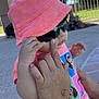 baby, child, toddler, pink_hat, sunglasses, hand, outdoor, sunny, concrete, fence, tattoo, clothing, person, cute, summer, casual, portrait, baby_girl, fashion, playful