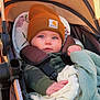 baby, child, stroller, blanket, hat, beanie, clothing, face, hands, blue_eyes, camouflage, carhartt, infant, outdoor, warm_clothing, cute, seated, comfort, portrait, young_child