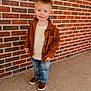boy, brick_wall, brown_jacket, brown_shoes, casual_clothing, child, concrete_floor, cream_shirt, cute, fashion, full_body, happy, outdoor, person, portrait, ripped_jeans, short_hair, smiling, standing, youth