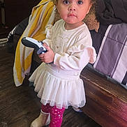 Valentina is registered to the contest to win money with this photo: toddler, child, indoor, game_controller, dress, bow, leggings, boots, bed, blanket, dresser, stickers, floor, wooden_floor, person, cute, pink, white, clothing, toy