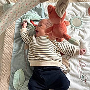 Nahil a rejoint le concours — aidez-le/la à gagner de superbes lots ! baby, infant, play_mat, plush_toy, striped_shirt, navy_pants, smiling, happy, child, soft_toys, floor, indoor, cute, cozy, playtime, clothing, person, baby_gym, mirror, embroidery
