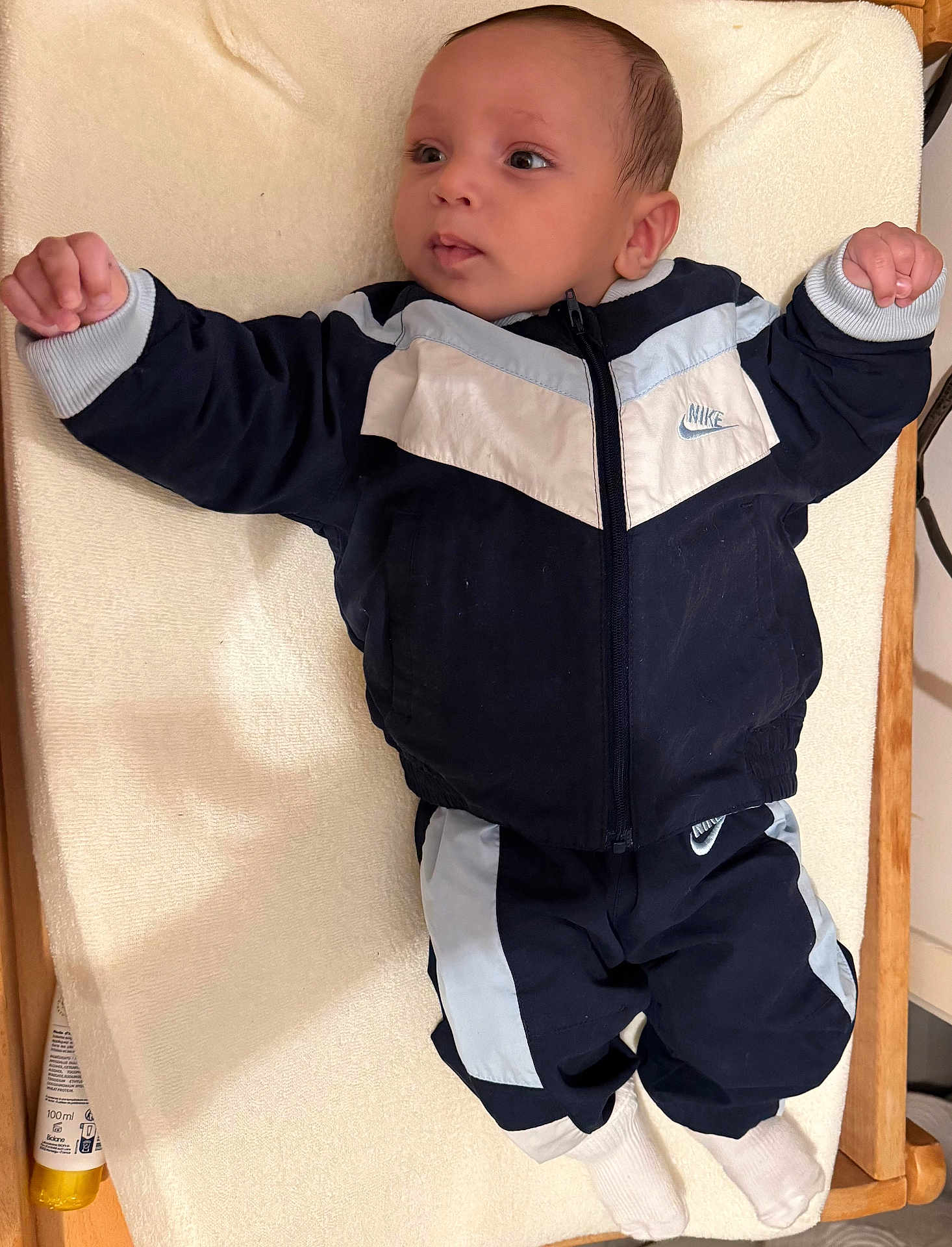 Nahil participe au concours pour gagner de l'argent avec cette photo : baby, infant, child, nike, tracksuit, clothing, socks, lying_down, changing_pad, wooden_frame, indoor, portrait, cute, face, expression, apparel, person, young_child, soft_fabric, resting