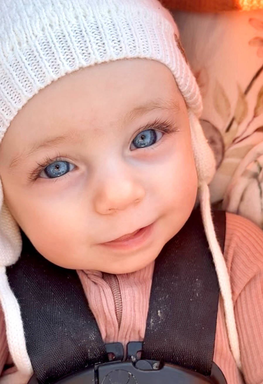 Norah is registered to the contest to win money with this photo: baby, cap, cheek, chin, eye, eyebrow, facial_expression, happy, head, headwear, iris, lip, nose, organ, outerwear, person, pink, skin, sleeve, smile