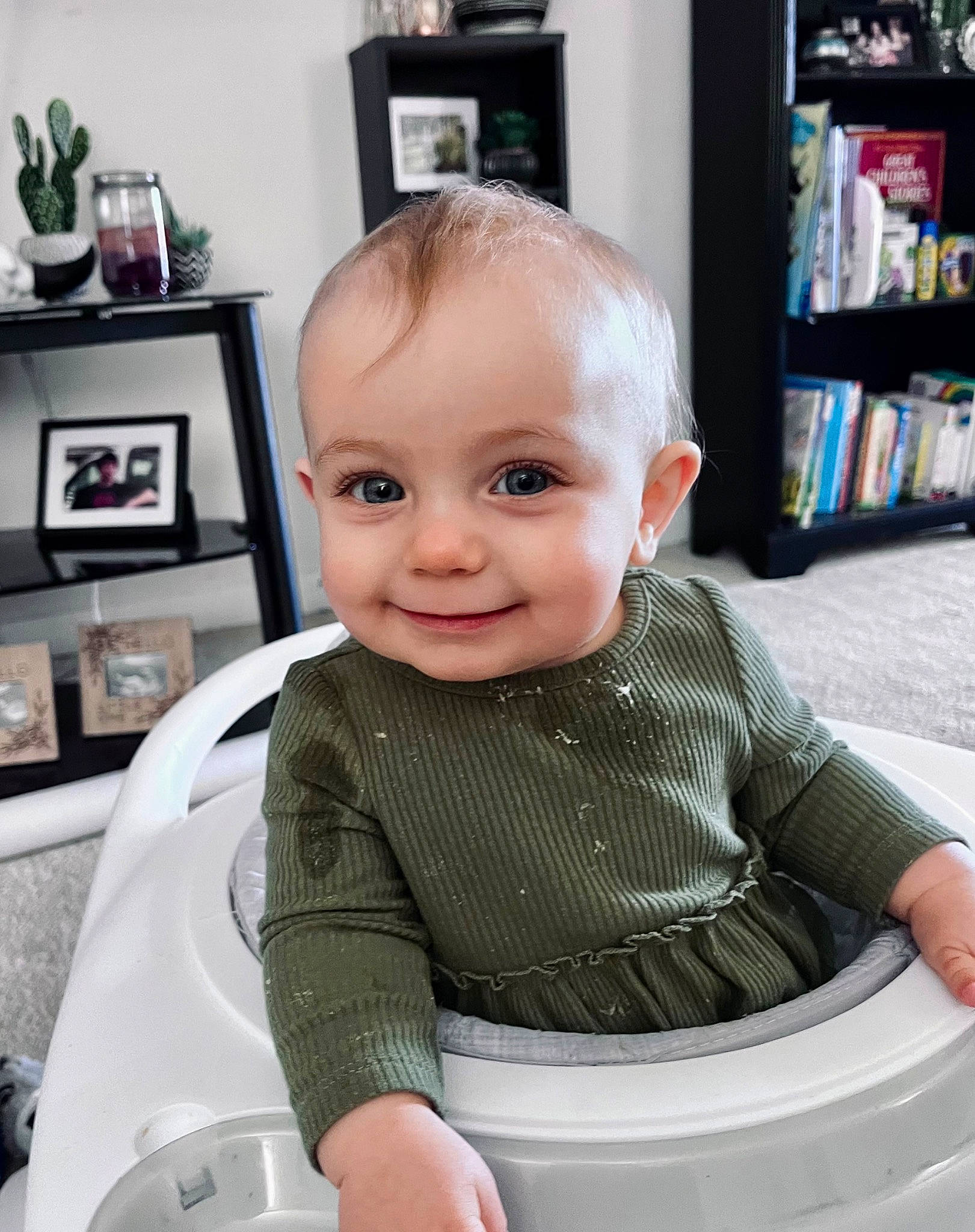 Anakyn is registered to the contest to win money with this photo: baby, baby_toddler_clothing, bookcase, cheek, child, flooring, fun, hair, hairstyle, happy, joy, person, picture_frame, plant, shelf, sitting, skin, sleeve, smile, t_shirt