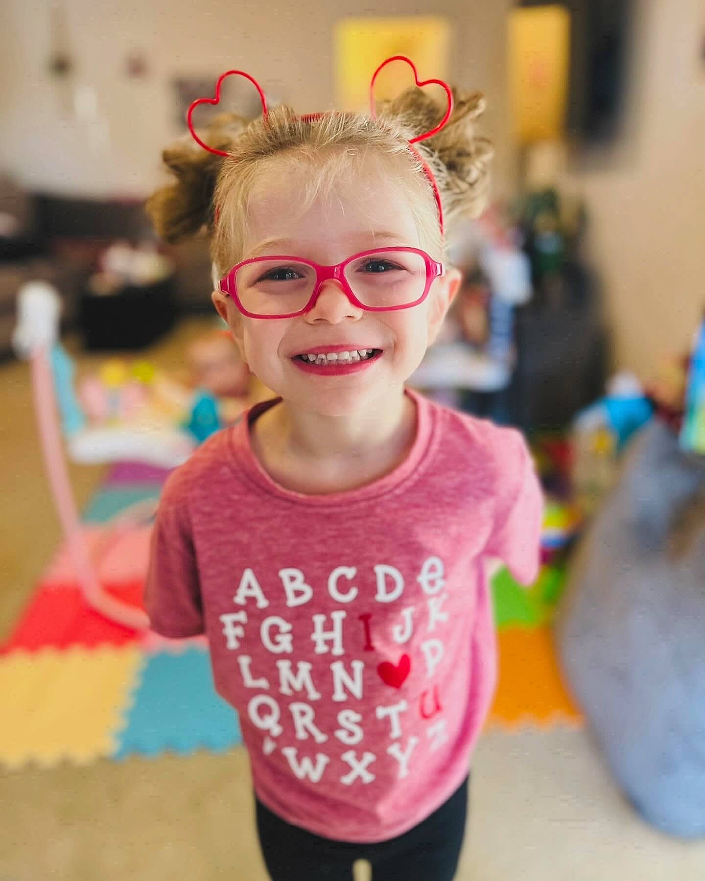 Austyn is registered to the contest to win money with this photo: child, event, eyewear, fashion_accessory, fun, glasses, hairstyle, happy, joy, kindergarten, leisure, magenta, party, person, personal_protective_equipment, pink, room, sleeve, smile, t_shirt