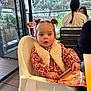 Alba participe au concours pour gagner de l'argent avec cette photo : toddler, child, high_chair, menu, pigtails, indoor, cafe, glass_wall, table, chair, person, red_flower_pattern, vest, wood_floor, people, braid, casual_clothing, window, daylight, expression