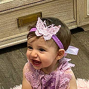 Harper is registered to the contest to win money with this photo: toddler, child, smiling, purple_dress, headband, butterfly, toy, ball, pink_rug, indoor, wooden_floor, wooden_furniture, happy, cute, portrait, baby, sitting, hands, face, young_child