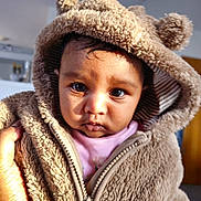 Aaria Sah Punj is registered to the contest to win money with this photo: baby, child, face, hood, jacket, fur, ears, hand, indoor, portrait, cute, warm_clothing, expression, young_child, closeup, soft_texture, person, looking, light, innocence