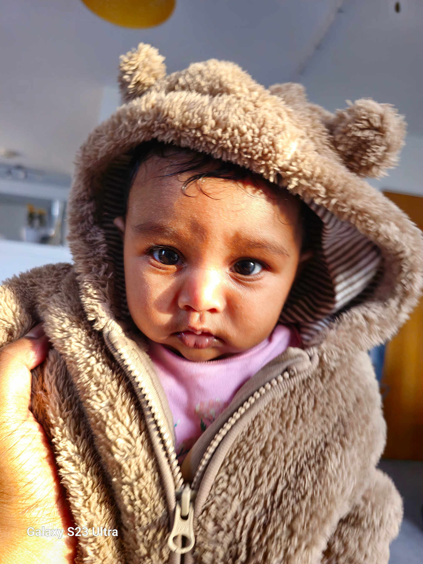 Aaria Sah Punj is registered to the contest to win money with this photo: baby, child, face, hood, jacket, fur, ears, hand, indoor, portrait, cute, warm_clothing, expression, young_child, closeup, soft_texture, person, looking, light, innocence