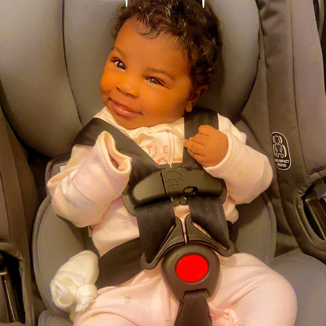 Legacy is registered to the contest to win money with this photo: baby, car_seat, child, smiling, pink_pajamas, infant, face, seatbelt, strapped_in, cute, indoors, winking, headrest, clothing, person, safety_harness, dove_graphic, text_overlay, happy, portrait