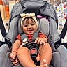 baby, car_seat, smile, headband, infant, child, happy, indoor, shopping, store, toy, seat_belt, foot, hand, clothing, person, cute, playful, accessory, fabric