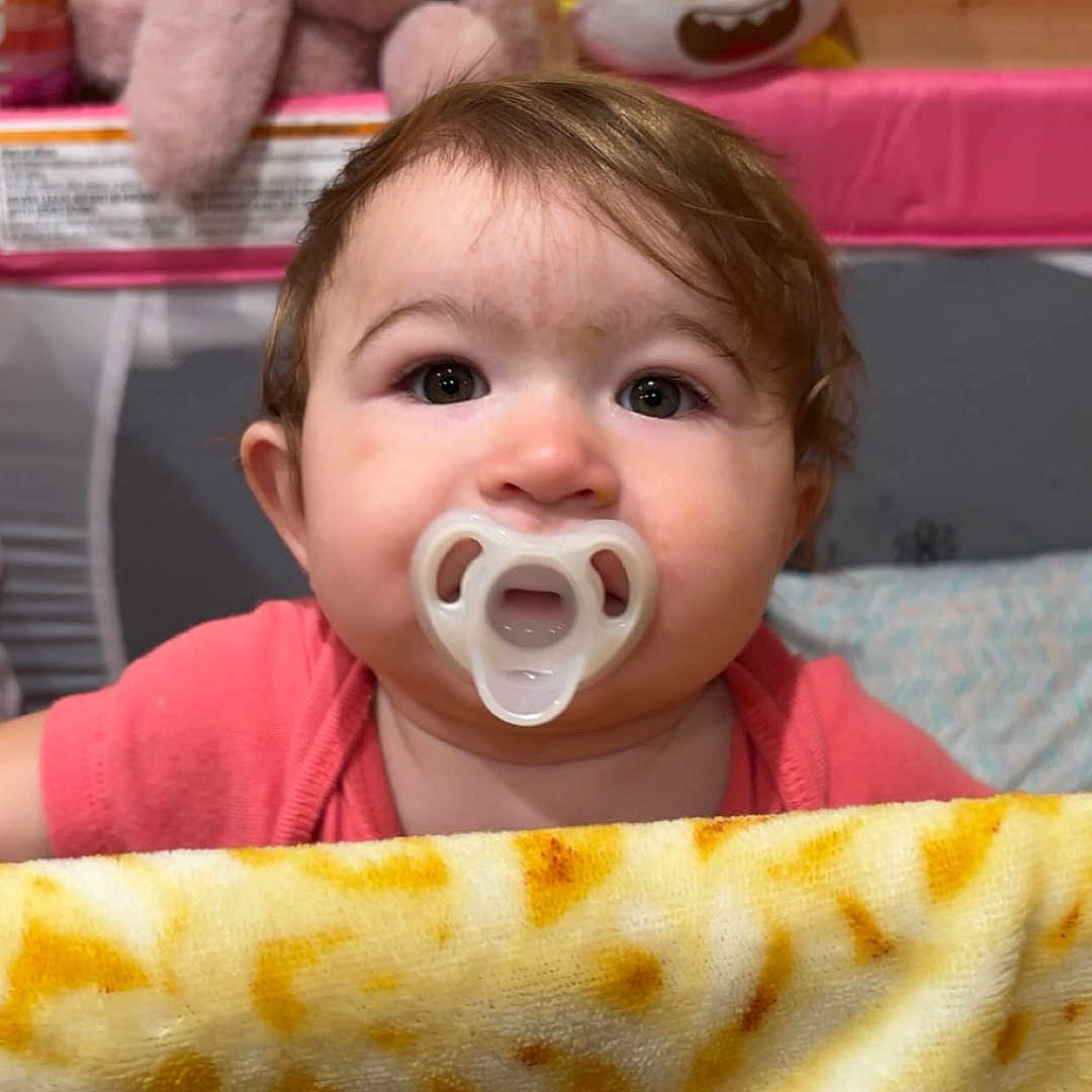 Isabelle joined the competition — help win amazing prizes! baby, pacifier, blanket, plush_toy, stuffed_bunny, yellow_toy, wooden_wall, pink_clothing, indoor, child, face, curly_hair, cute, infant, soft_toy, bedroom, playpen, expression, childhood, toy