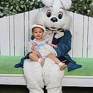 Nita is registered to the contest to win money with this photo: bench, bunny_costume, child, costume, family_event, fence, floral_background, flowers, grass, green_cushion, hat, holiday_photo, mascot, outdoor, person, plush, portrait, sitting, smile, toddler