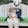 Nita is registered to the contest to win money with this photo: bench, bunny_costume, child, costume, family_event, fence, floral_background, flowers, grass, green_cushion, hat, holiday_photo, mascot, outdoor, person, plush, portrait, sitting, smile, toddler