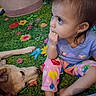 child, toddler, dog, pet, sitting, curious, play_mat, colorful, flowers, indoor, portrait, candid, brown_hair, purple_shirt, pink_pants, rainbow, animal, companion, floor, family
