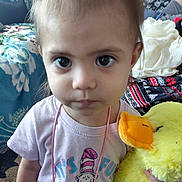 Nita is registered to the contest to win money with this photo: toddler, child, plush_toy, yellow_duck, indoor, person, pink_shirt, big_eyes, curious_expression, toy, couch, blanket, patterned_fabric, home, soft_toy, young_child, portrait, cute, casual_clothing, living_room