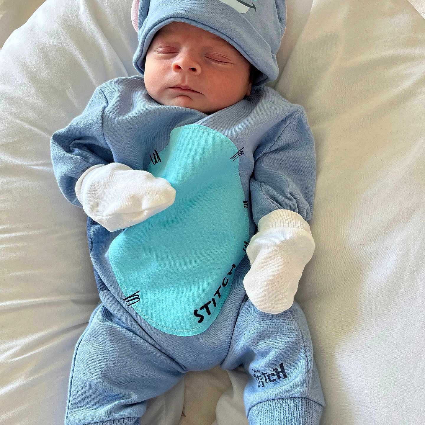 Alfie is registered to the contest to win money with this photo: baby, babywear, blue_outfit, child, clothing, comfortable, cute, disney, hat, indoors, infant, mittens, newborn, peaceful, portrait, resting, sleeping, soft_blanket, stitch, white