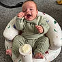 baby, infant, knitted_clothing, sitting, smiling, happy, inflatable_chair, carpet, indoor, container, foot, hand, face, cute, child, young, cozy, playful, joyful, home