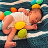 newborn, baby, smiling, sleeping, blanket, knitted_blanket, easter_eggs, colorful, plastic_eggs, infant, cute, small, lying_down, soft_texture, cozy, resting, happy, child, indoors, portrait