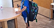 King joined the competition — help win amazing prizes! child, boy, backpack, blue_shirt, shorts, sneakers, toy, cup, table, indoor, floor, chair, smile, hair, standing, person, wall, door, carpet, furniture