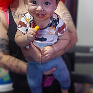 King is registered to the contest to win money with this photo: adult, baby, blue_pants, blurred_background, candid, child, clothing, family, happy, holding, human, indoor, messy_face, person, portrait, red_hair, short_sleeve_shirt, smiling, snack, tattoo