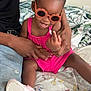 Maleah is registered to the contest to win money with this photo: toddler, child, sunglasses, pink_outfit, smiling, adult, hands, bedspread, floral_pattern, indoor, happy, person, footwear, jeans, casual, hair_buns, playful, seated, cute, accessories