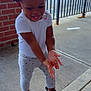 toddler, child, smiling, clapping, white_shirt, heart_patterned_leggings, black_shoes, outdoor, sidewalk, brick_wall, metal_railing, parking_lot, cars, happy, cute, standing, daylight, playful, young_child, person